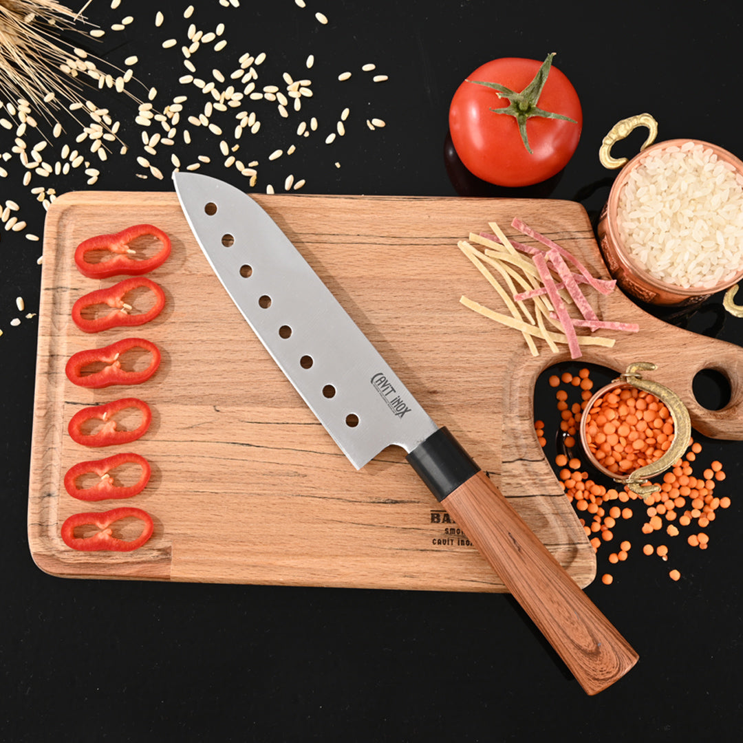 Cavit İnox Asya Serisi delikli santoku şef bıçağı, siyah fonda ahşap tahtada domates dilimleri ve mercimekle